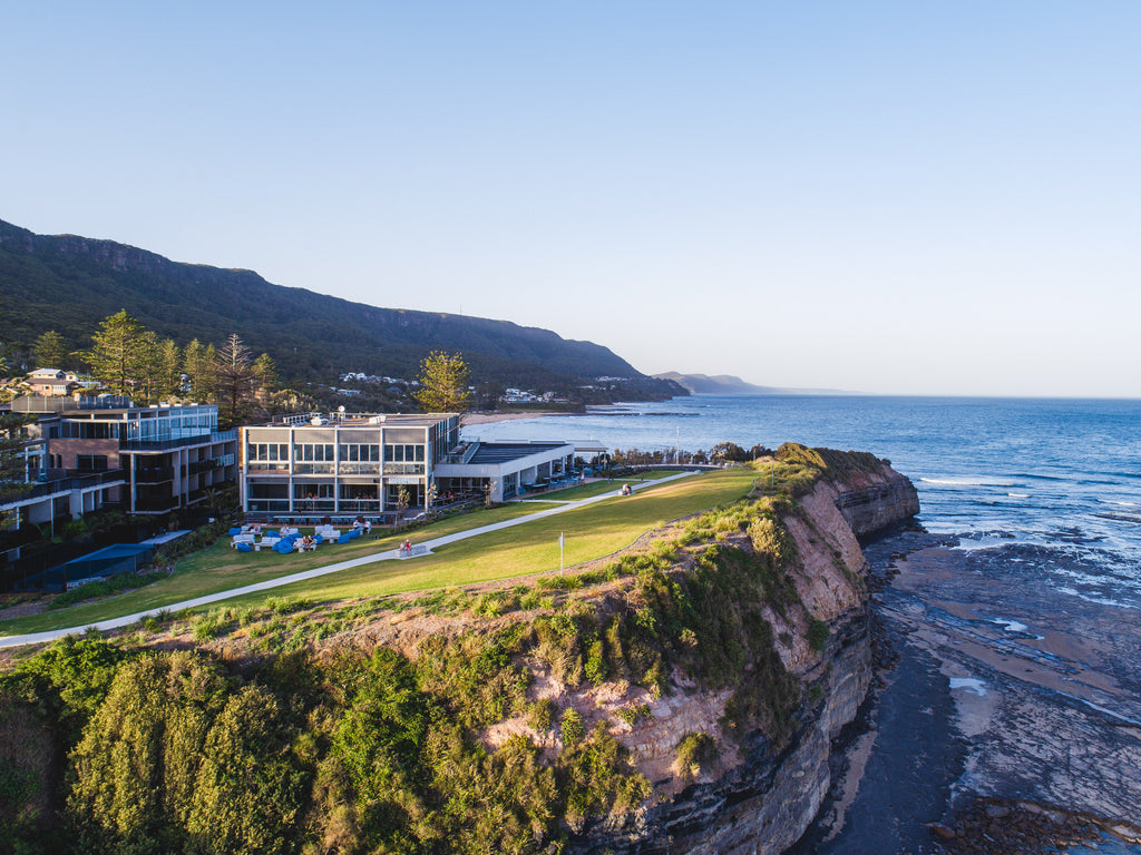 Coastal landscape with buildings, grassy area, and ocean.