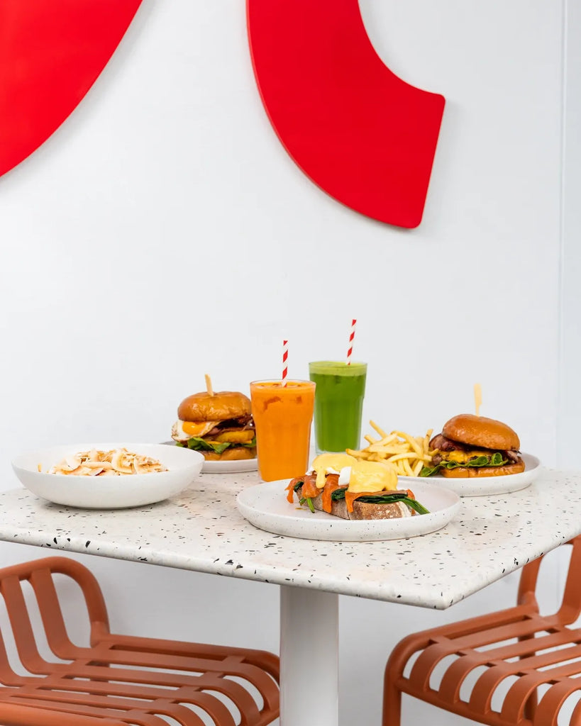 Dining table with burgers, drinks, and snacks in a modern setting with red abstract art on the wall.