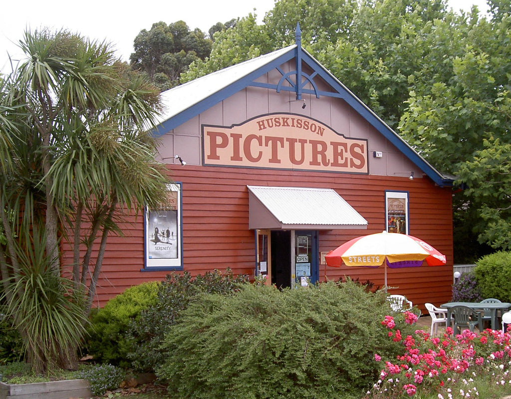 Red building with 'Huskisson Pictures' sign, surrounded by greenery and flowers