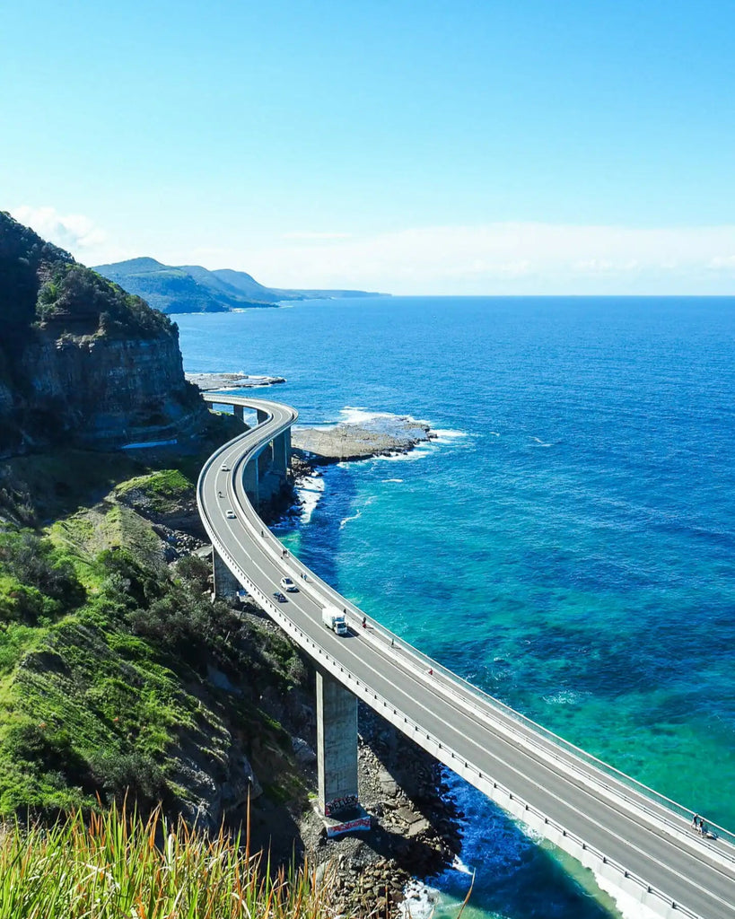 Road along a cliff overlooking the ocean with clear blue water and sky.