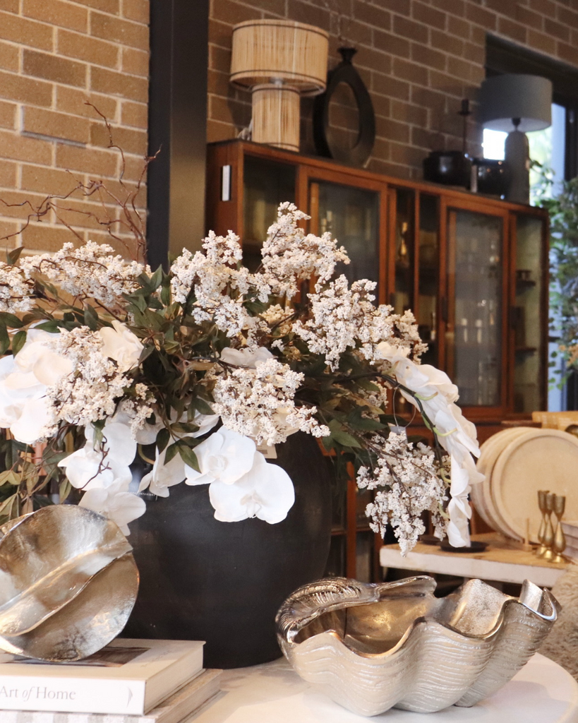 Decorative arrangement with flowers and bowls on a table against a brick wall.
