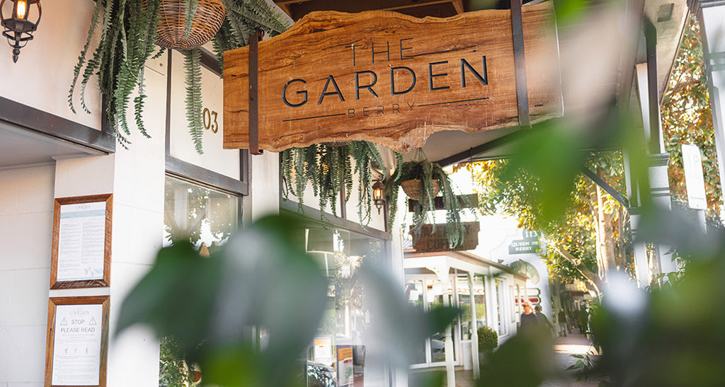 Wooden sign reading 'The Garden' with greenery around, indicating a restaurant or cafe entrance.