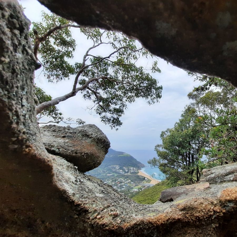 Scenic view through rocky outcrop with trees and a body of water in the distance.