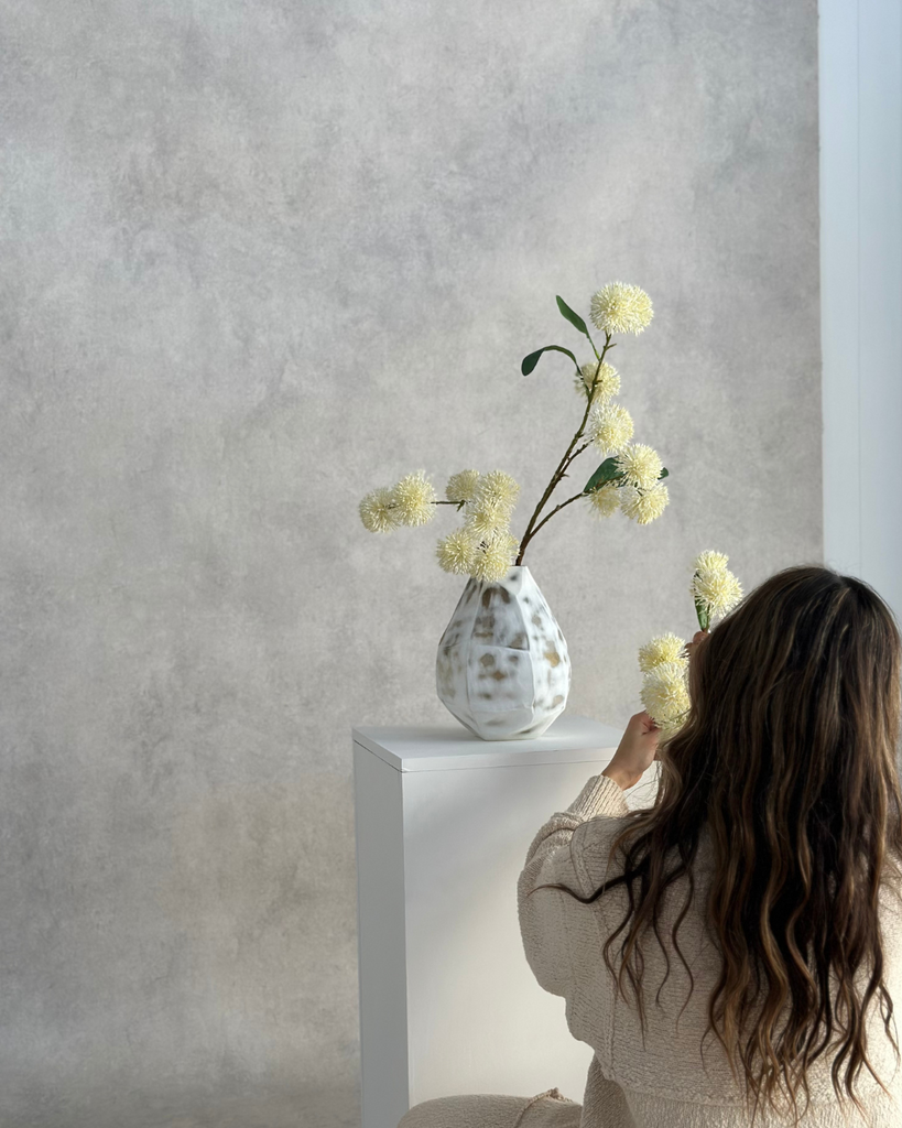 Woman arranging flowers in a vase against a plain wall