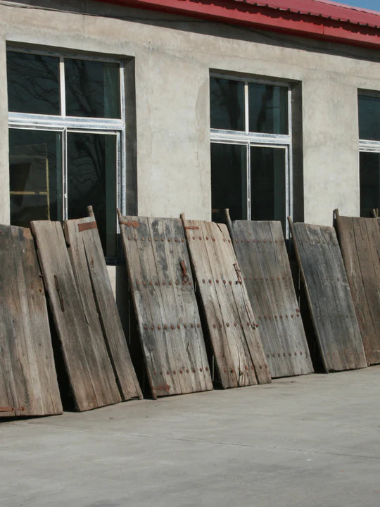 Wooden antique doors leaning against a building with a red roof in Northern China.