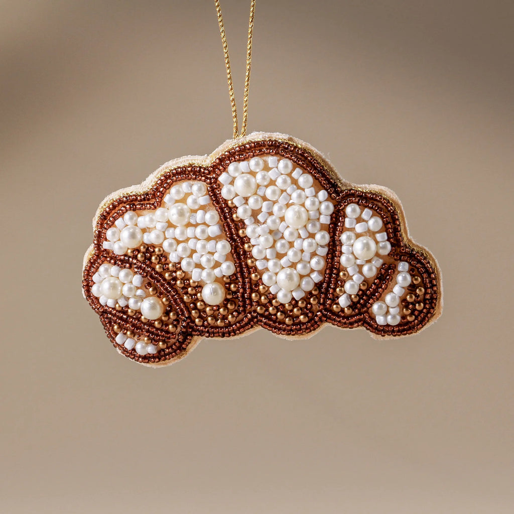 Decorative croissant ornament with pearl-like beads on a beige background