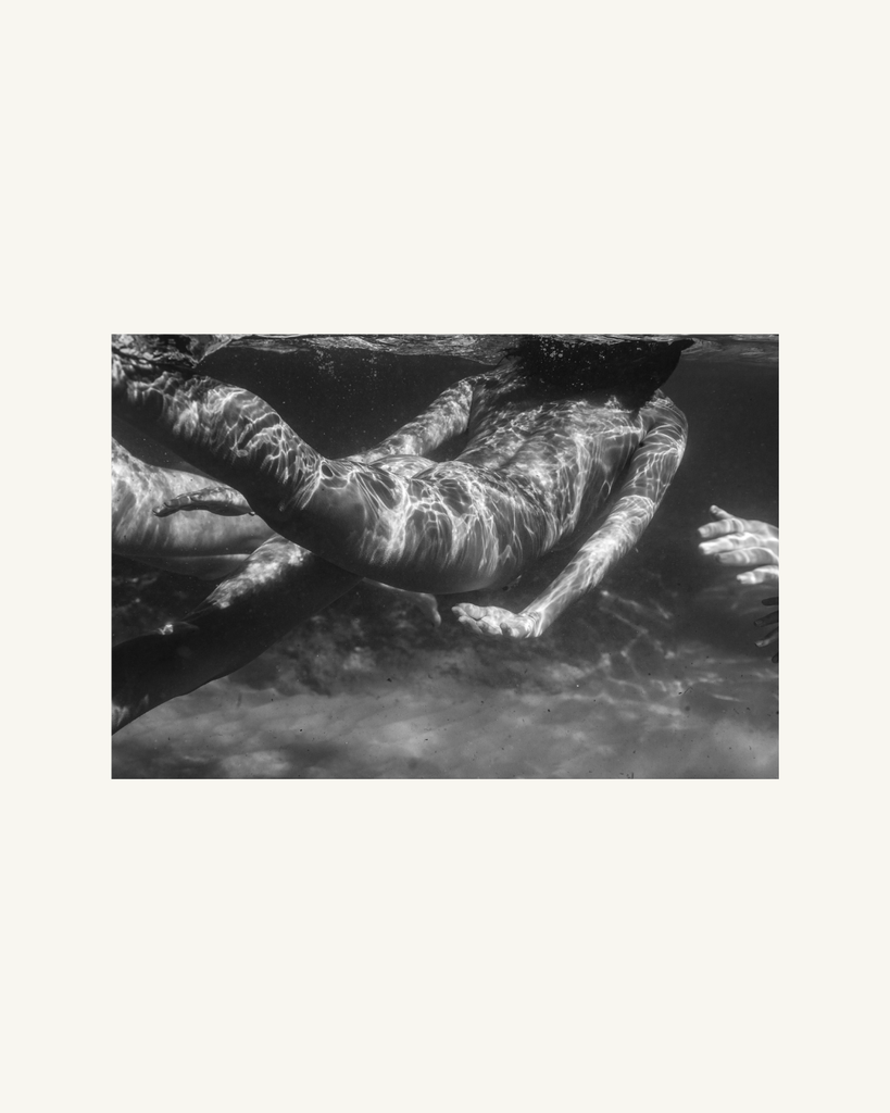Black and white photo of a person underwater with sunlight filtering through.