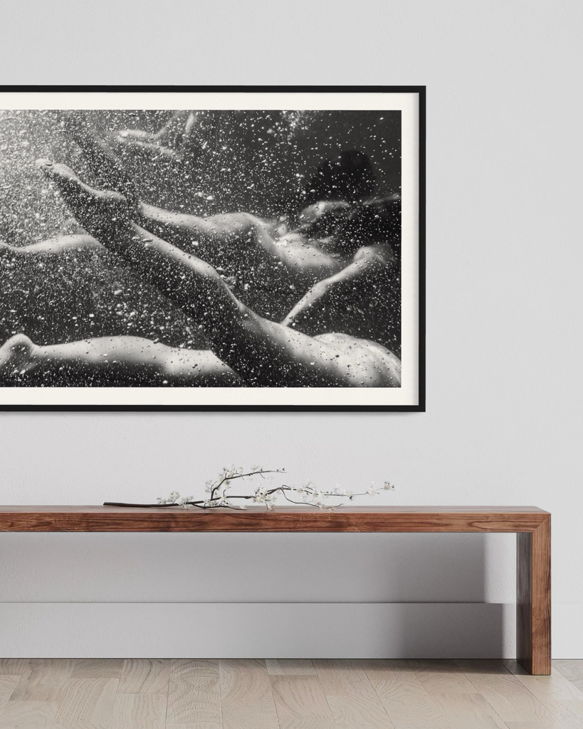 Framed black and white artwork of a nude figure underwater on a wall above a wooden console table.