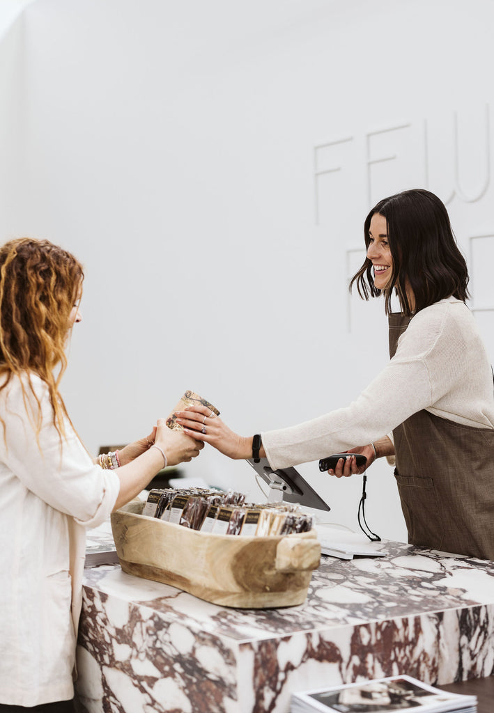 Two women interacting over a table with a decorative box on a white wall background