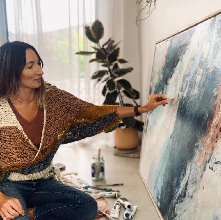 Woman painting a large abstract artwork in a bright room with plants.