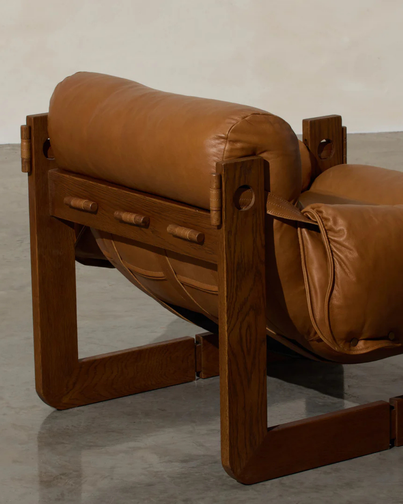 Brown leather chair with wooden frame on a gray floor.
