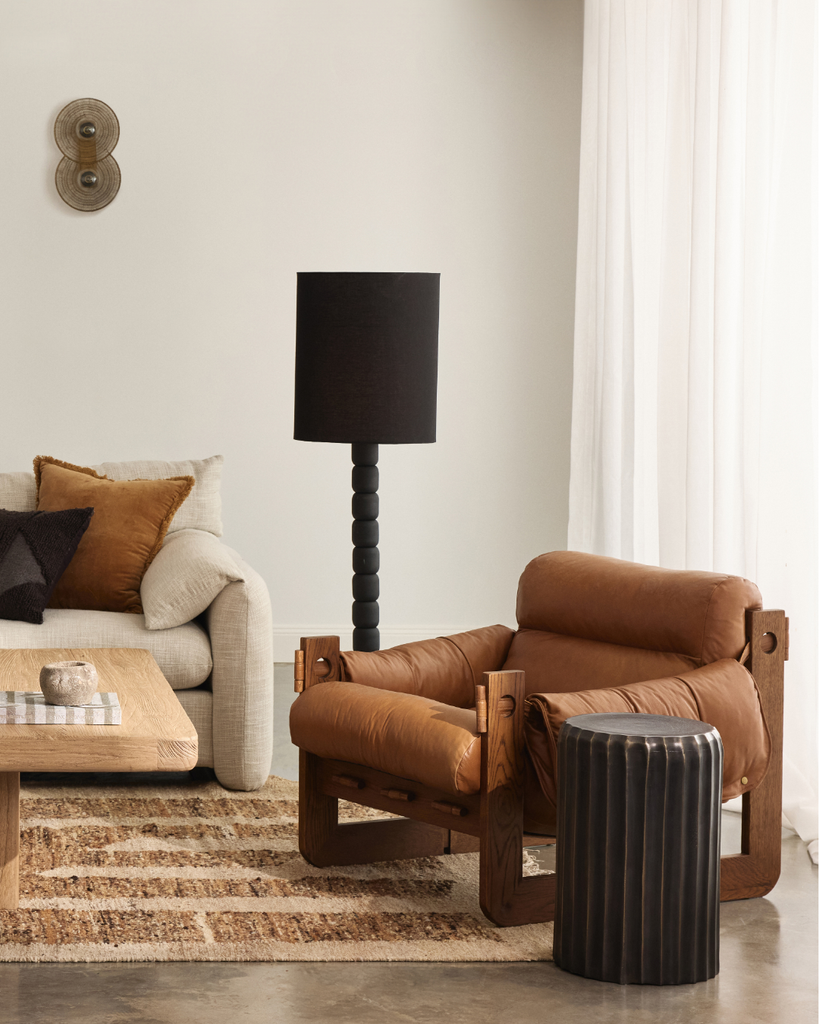 Modern living room with a brown leather armchair, beige sofa, and black lamp.