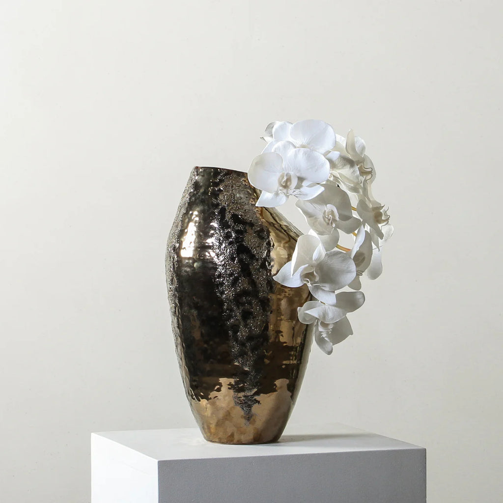 Decorative vase with textured surface and white flowers on a light gray background