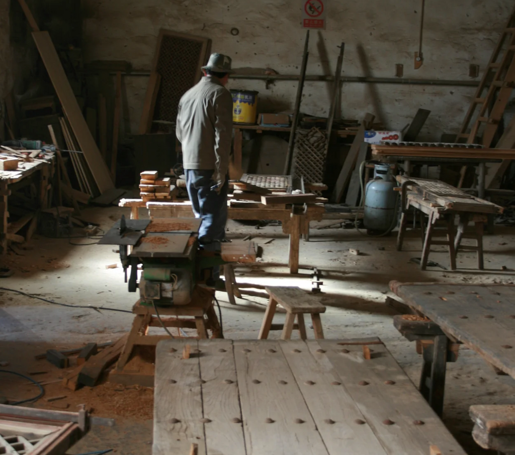 Man working in an antique workshop with tools and materials scattered around.