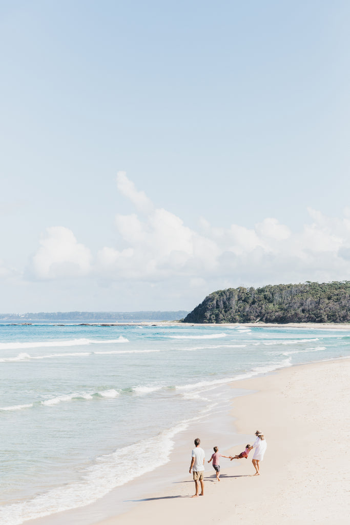 Two adults and children walking along a sandy beach with ocean and sky in the background