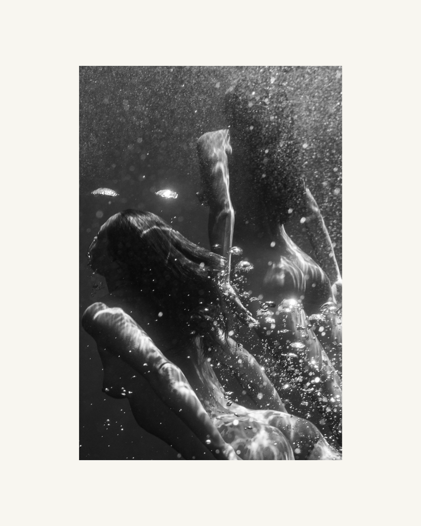 Black and white underwater scene with hands reaching towards each other.