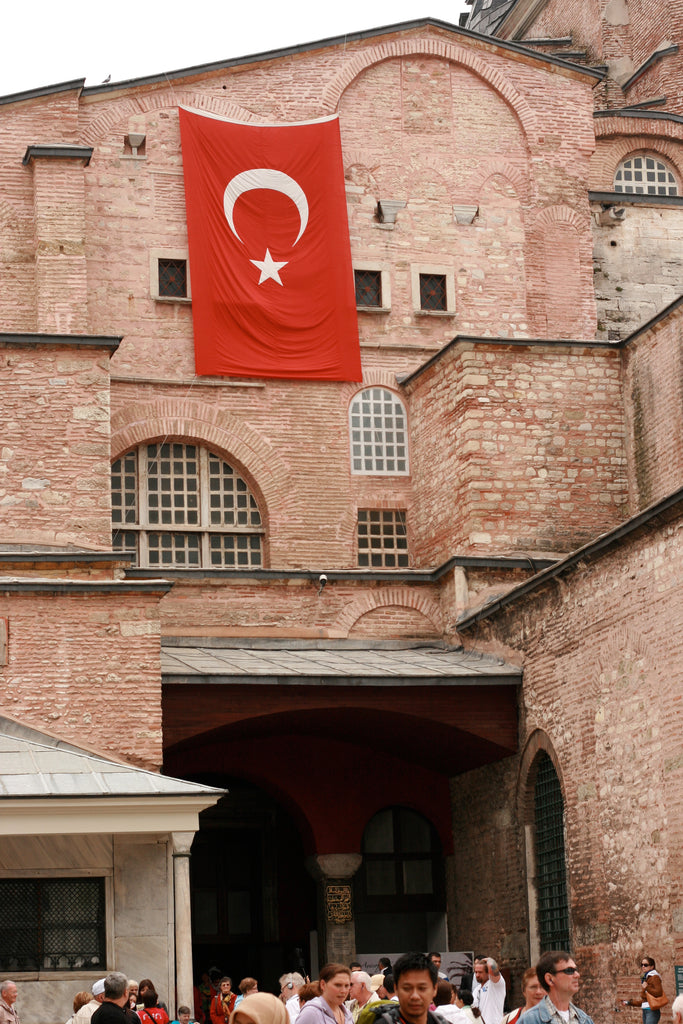 Turkish flag hanging from a historic brick building with people below.