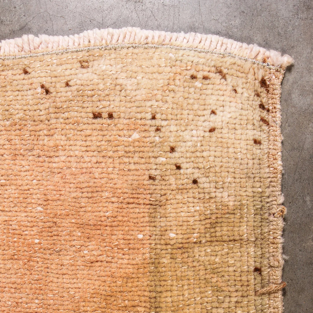 Close-up of a textured beige vintage Turkish rug corner on a concrete floor.
