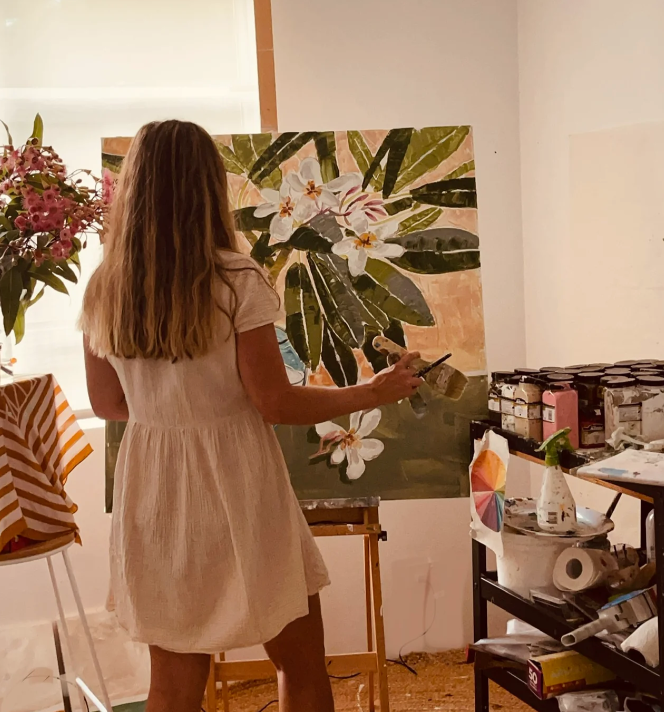Woman painting a floral scene on an easel in a studio setting.