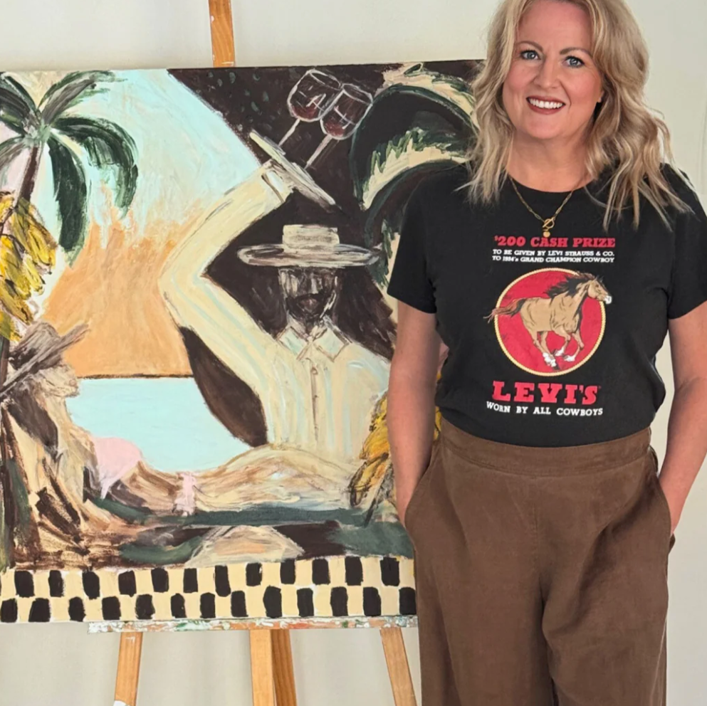 Woman wearing a Levi's t-shirt standing next to a painting on an easel.